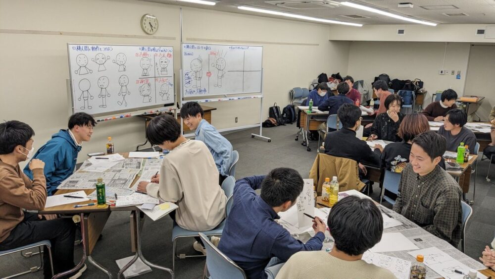 会議室で、参加者が机を囲み、描いた棒人間を見せ合って、笑顔で話している様子