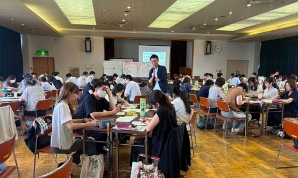 大きなホールで、多くの参加者がグループになって、紙に描きながら話し合っている様子