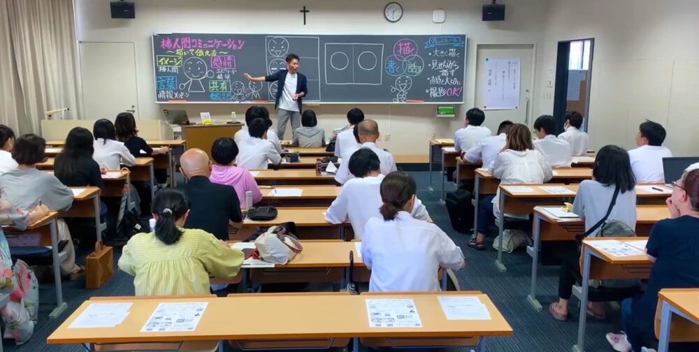 教室で、講師が黒板に描いた棒人間を使って、参加者に描き方と伝え方を説明している様子